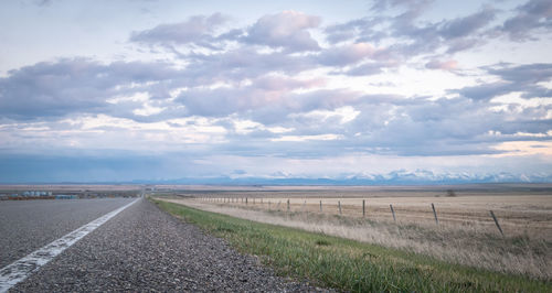 Empty road amidst field against sky