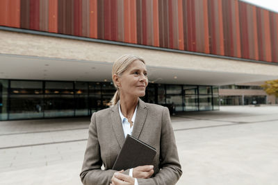 Blond businesswoman holding tablet pc on footpath