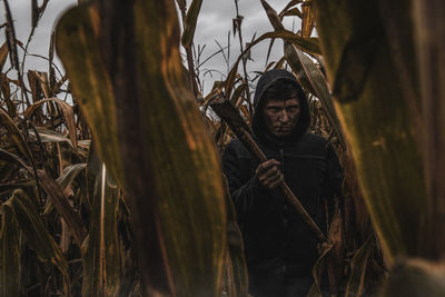 Portrait of angry man with axe standing amidst corns on farm