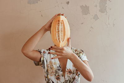 Woman covering face with sliced vegetable against wall at home