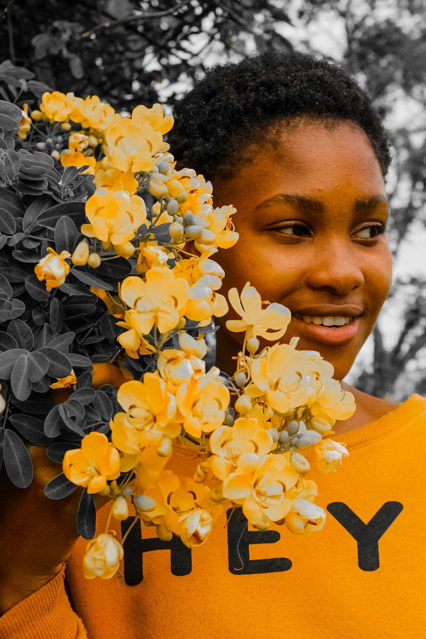 yellow, flowering plant, flower, one person, plant, portrait, smiling, nature, happiness, women, emotion, beauty in nature, looking at camera, headshot, spring, cheerful, adult, child, front view, lifestyles, young adult, childhood, freshness, holding, outdoors, flower head, close-up, leisure activity, female, person, black hair, autumn