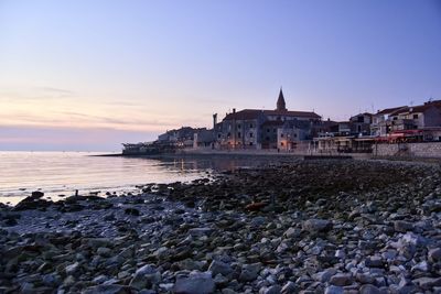 Sea and buildings against sky at sunset