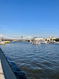 Bridge over river in city against clear blue sky