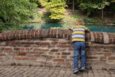 Rear view of boy standing against brick wall