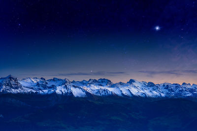 Scenic view of snowcapped mountains against blue sky at night