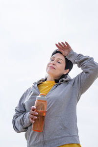 Low angle view of young woman drinking drink against sky