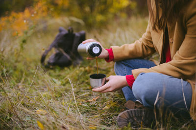 Low section of woman pouring tea in cup on field