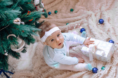 High angle view of girl with gift by christmas tree on carpet