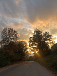 Road amidst trees against sky during sunset