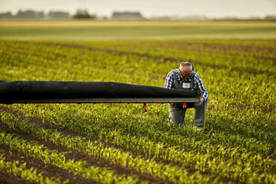 Farmer adjusting crop sprayer in field at sunset