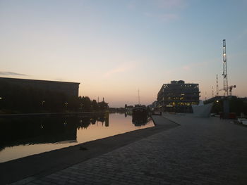 Buildings by river against sky at sunset