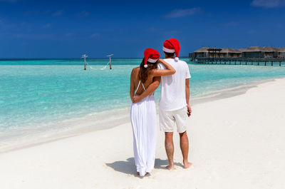 Rear view of couple standing on beach against sky