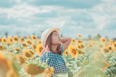 Young woman by sunflowers against sky