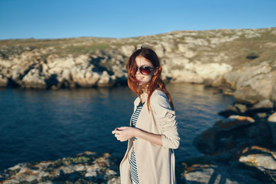 Portrait of young woman wearing sunglasses standing against sky