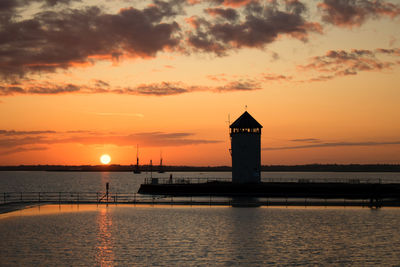 Silhouette lighthouse by sea against orange sky