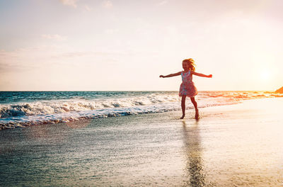 Girl with arms outstretched standing at beach during sunset