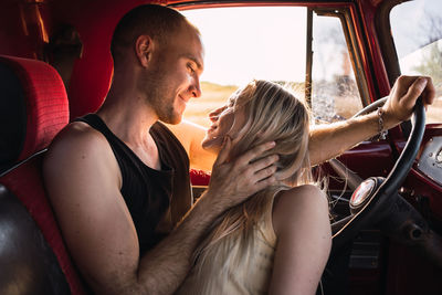 Loving couple looking at each other in vintage car parked in nature on sunny day