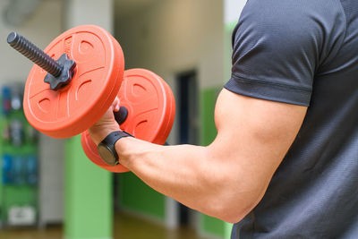 Midsection of man lifting dumbbell in gym