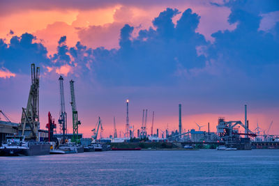 Cranes at commercial dock against sky during sunset