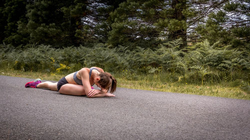 Full length of woman exercising while sitting on road