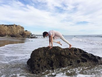 Woman practicing yoga at beach against sky