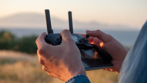 Cropped hands holding drone remote control against sky