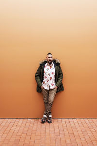 Young bearded man with hands on pocket leaning on wall, looking camera