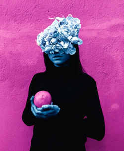 Midsection of woman holding pink flower against wall