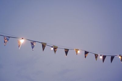 Low angle view of bunting flags with illuminated light bulbs against sky at dusk