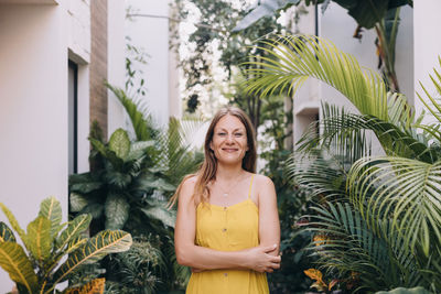 Portrait of young caucasian woman looking at camera, standing against tropical plants