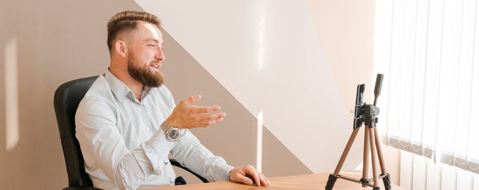 Cheerful bearded young man leading an online meeting using smartphone writing