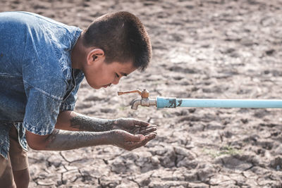 Boy with dirty hands under tap on drought land