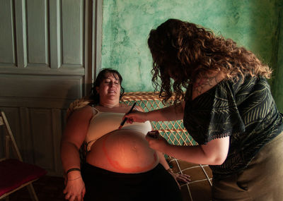 Woman painting on pregnant belly at home