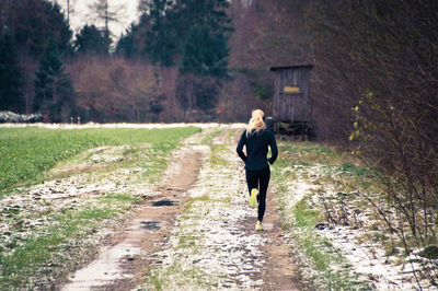Rear view of woman running on field during winter