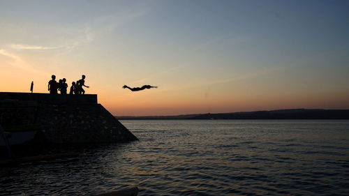 Silhouette people in sea against sky during sunset