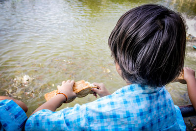High angle view of boy eating bread while sitting in boat on lake