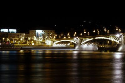 Illuminated bridge over river in city at night