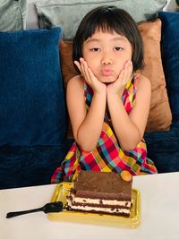 Portrait of cute girl with cake on table sitting at home