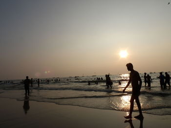 People walking on beach against sky during sunset