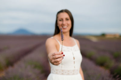 Portrait of smiling woman holding plant standing at field