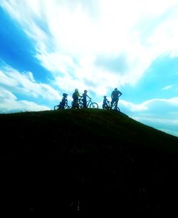 Silhouette people on bicycle against sky