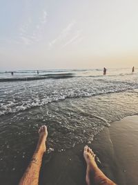 Low section of people on beach against sky