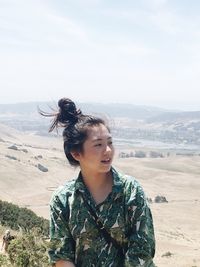 Young woman looking away while standing on mountain against sky during sunny day