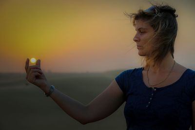 Optical illusion of woman holding sun during sunset