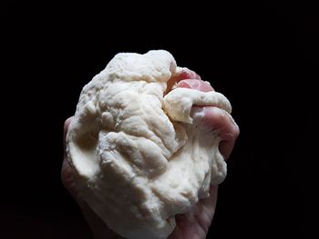 Cropped hand holding dough against black background