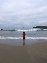 Rear view of woman standing at beach against sky