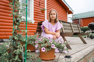 Portrait of young woman sitting by potted plant