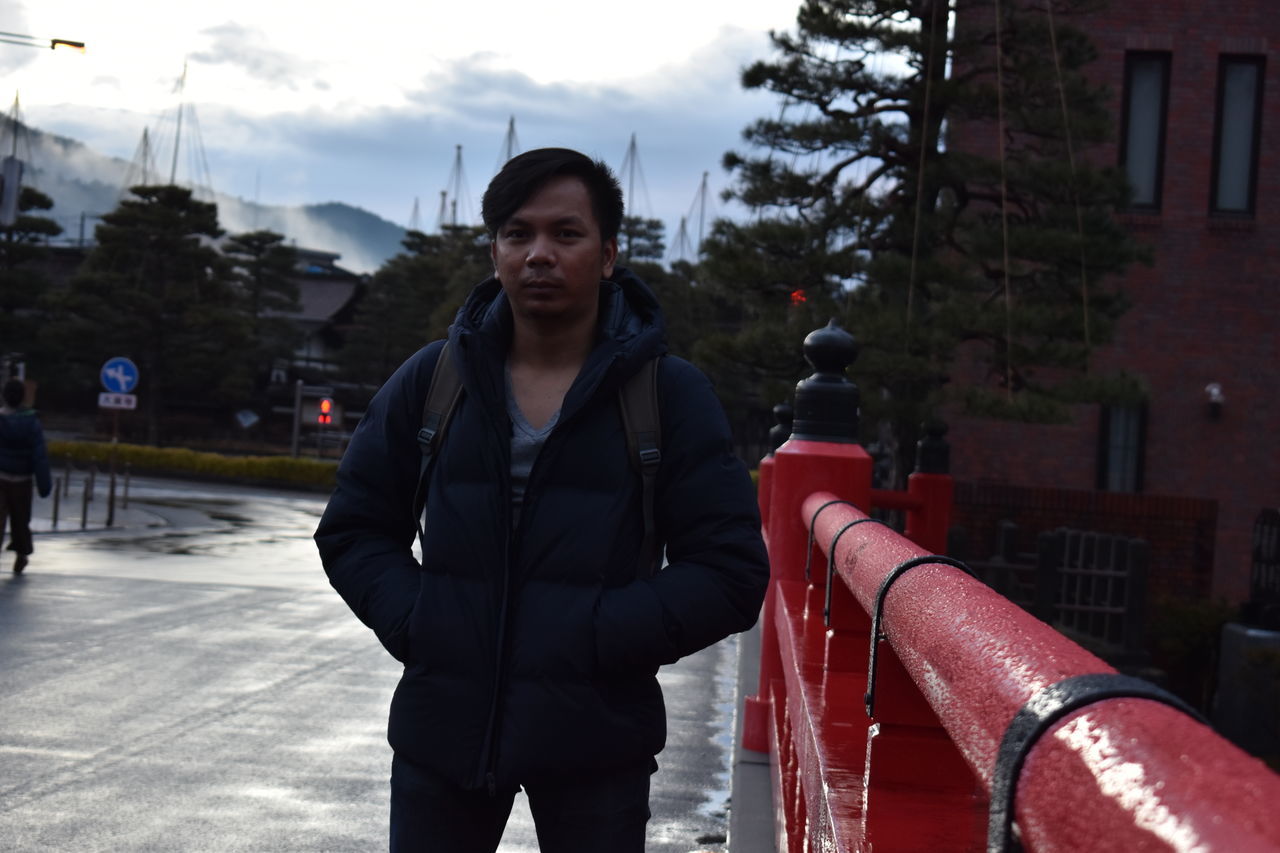 YOUNG MAN STANDING IN CITY AGAINST SKY