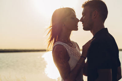 Side view of couple romancing against lake at sunset