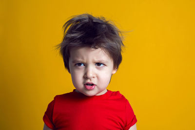 Cheerful baby boy in red t-shirt stands on yellow background